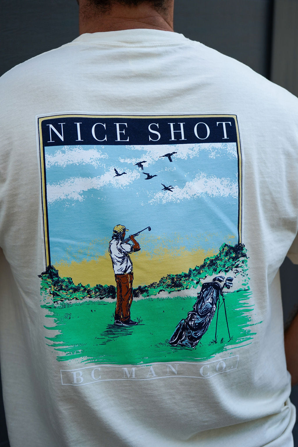 Back view of the BC Man Co Nice Shot Tee in ivory showing golfer shooting at ducks over the fairway